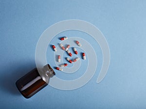 Pills spilling from a amber bottle, on blue paper background. Top view