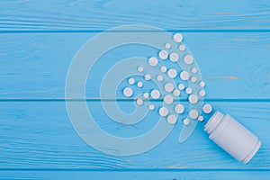 Pills spilling out of a bottle on blue wooden table.