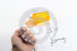Pills Spilling out of Bottle near Womans hand near sorry note, implication suicide overdose, posed studio shot