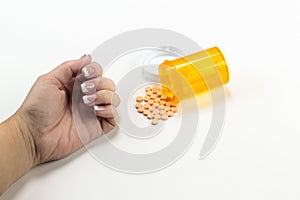 Pills spilling out of bottle near womans hand with white cap implying overdose suicide