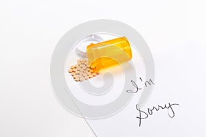 Pills spilling out of medicine bottle with I'm Sorry note, implication suicide overdose photo