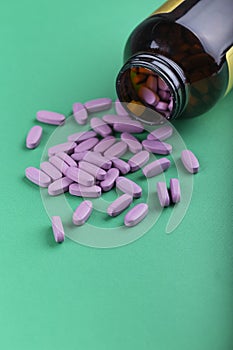 Pills spilling out of pill bottle and isolated on green. Top view with copy space