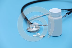 Pills spilling out of pill bottle syringe thermometer and stethoscope on blue background. selective focus