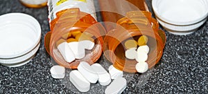 Pills spilling out of two prescription pill bottles on a black counter