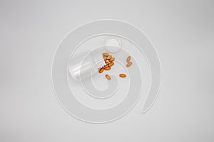 Pills spilling out of a white pill bottle against a white background