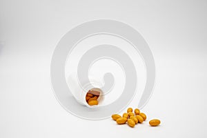 Pills spilling out of a white pill bottle against a white background