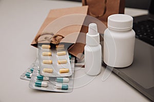 Pills and spray containers and buff paper bags near laptop close-up. Online pharmacy concept