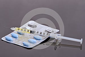 Pills, syringe and needle on grey background