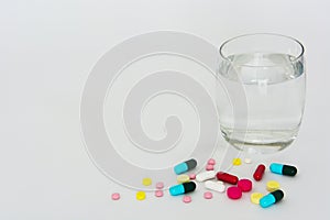 Pills and tablets of medicine with glass of drinking water isolated on white background