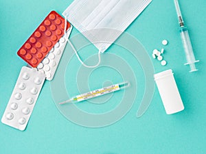 Pills, thermometer, medical face mask, syringe on a blue background, top view