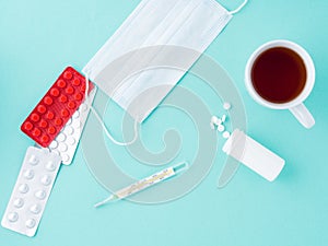 Pills, thermometer, medical face mask, tea in a mug on a blue background