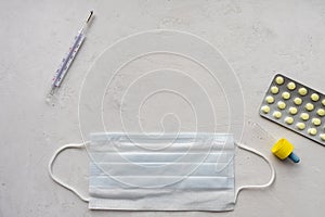 Pills, thermometer and protective medical mask on a gray background