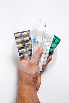 Pills for various diseases, a thermometer and a syringe in a personâ€™s hand