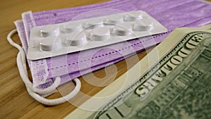 Pills in white plastic, medical masks and dollars on the table.