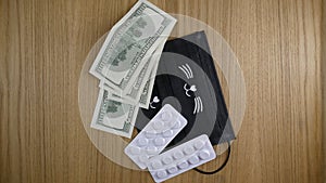 Pills in white plastic, medical masks and dollars on the table.