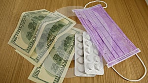 Pills in white plastic, medical masks and dollars on the table.