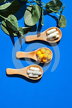 Pills on wooden spoon on blue background. Hard light and shadows. Creative minimalism concept. Vitamins and prebiotics, probiotics photo