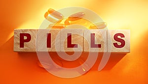 Pills word on wooden cubes with oil capsules around on orange background. Medical healthcare concept