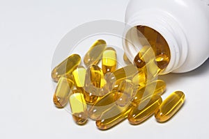 Pills of yellow color are poured on a white surface from plastic jar.