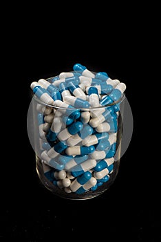 Pillules de mÃÂ©dicaments blanche et bleu dans un verre sur un fond noir photo