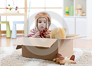 Pilot aviator baby with teddy bear toy and planes plays in cardboard box