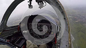 The pilot hold and control helm. A gray training aircraft fly over field and turns in the air. A fighter moves over a green forest