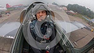 The pilot open helmet and looks around. Gray blue fighter combat aircraft ride the runway at old airfield on a cloudy day