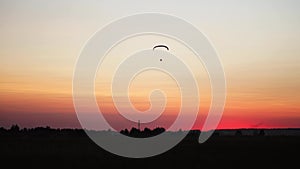 The pilot on a paraglider flies from the camera gradually moving away into the distance against the sunset beautiful sky