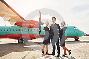 Pilot and two stewardesses. Crew of airport and plane workers in formal clothes standing outdoors together