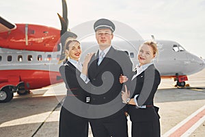 Pilot and two stewardesses. Crew of airport and plane workers in formal clothes standing outdoors together