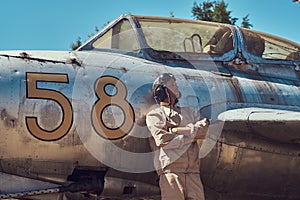 Pilot in uniform and flying helmet standing near an old war fighter-interceptor in an open-air museum.