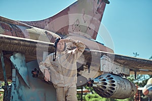 Pilot in uniform and flying helmet standing near an old war fighter-interceptor in an open-air museum.