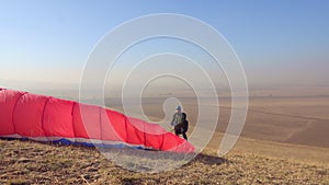 The pilot is waiting for a fair wind to take off on a red paraglider.