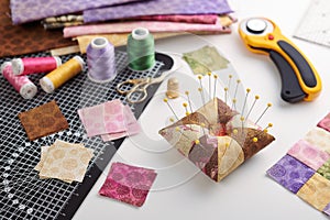 Pin cushion, stacks of square pieces of fabric, pile of patchwork fabrics, quilting and sewing accessories