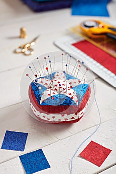 Pin cushion stylized elements of American flag, stacks of fabrics, quilting accessories