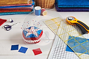 Pin cushion stylized elements of American flag, stacks of fabrics, quilting accessories