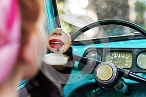 Pin-up girl is doing makeup in old car.