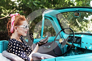 Pin-up girl is doing makeup in old car.