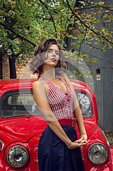 Pin-up girl posing on a red russian retro car background. Playful gaze fixed on camera.