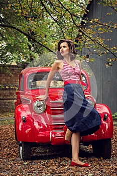 Pin-up girl posing on a red russian retro car background. A playful interested look is cast aside.