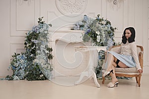 Pin up girl at a retro white apartment near the table. Pretty vintage woman in stylish room with flowers alone.