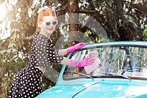 Pin-up girl in vintage clothes is washing mint old car.