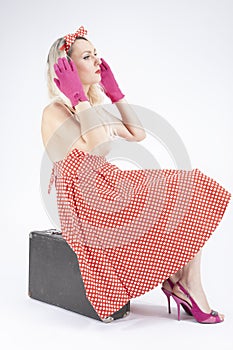 Pin-Up Ideas. Blond Girl in Pin-up Style Sitting on Suitcase Against White