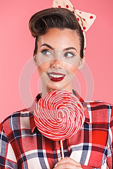 Pin-up woman isolated over pink background holding candy lollipop.