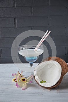 Pina colada drink in cocktail glass decorated with coconut and orchid flowers