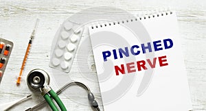PINCHED NERVE is written in a notebook on a white table next to pills and a stethoscope