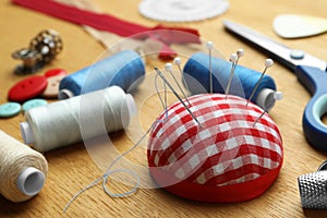 Pincushion, spools of threads and sewing tools on wooden table, closeup