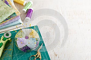 Pincushion, stack of fabrics, sewing and quilting accessories lying on a cutting mat, space for text