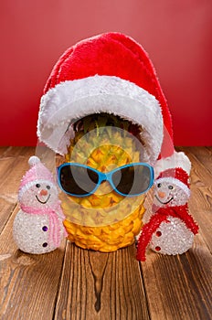 Pine apple wears a santa claus hat and sun glasses with two snowmen