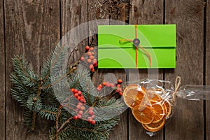 Pine branch and viburnum a bag with dried oranges and a green envelope with a gift lie on an old wooden background, new